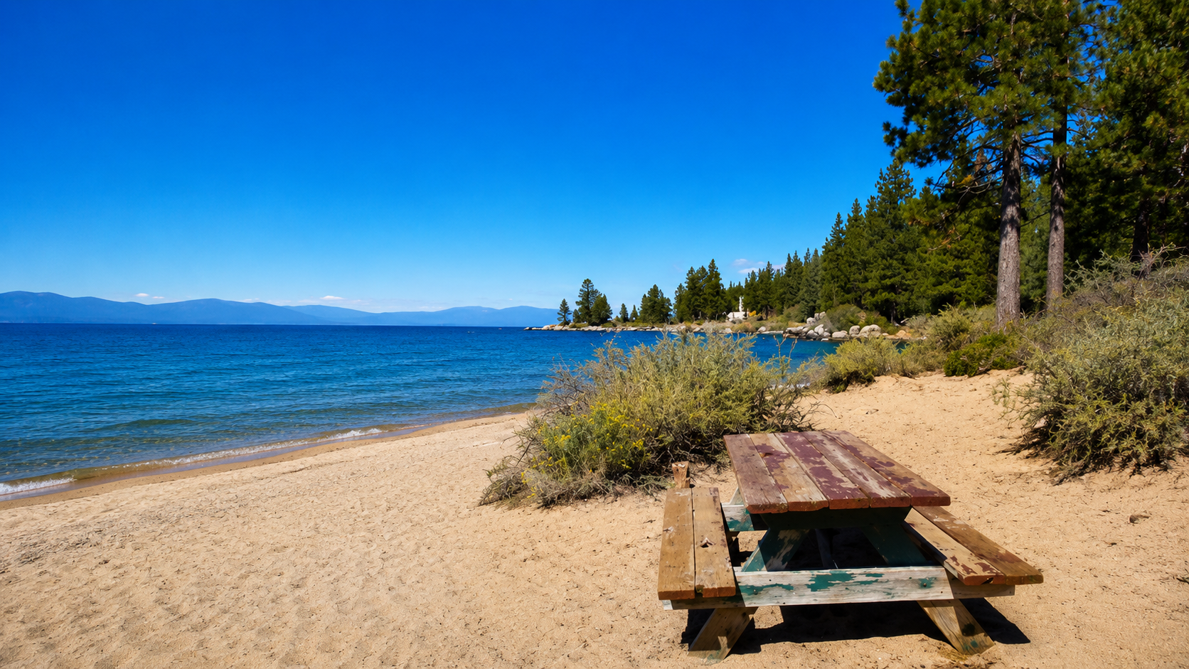 Weathered picnic table on the sandy beach at Zephyr Cove with pines and blue water
